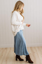 BLONDE WOMAN WEARING A HIGH-LOW HEM, LONG SLEEVE, SUPER SOFT, OVERSIZED CREW NECK SWEATER WITH RIB DETAILS AND STANDING IN A STUDIO WITH LIGHT WOOD FLOOR AND PANELED WALL BEHIND.