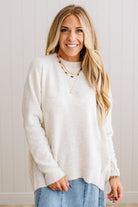BLONDE WOMAN WEARING A HIGH-LOW HEM, LONG SLEEVE, SUPER SOFT, OVERSIZED CREW NECK SWEATER WITH RIB DETAILS AND STANDING IN A STUDIO WITH LIGHT WOOD FLOOR AND PANELED WALL BEHIND.