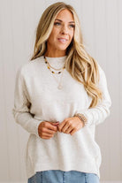 BLONDE WOMAN WEARING A HIGH-LOW HEM, LONG SLEEVE, SUPER SOFT, OVERSIZED CREW NECK SWEATER WITH RIB DETAILS AND STANDING IN A STUDIO WITH LIGHT WOOD FLOOR AND PANELED WALL BEHIND.