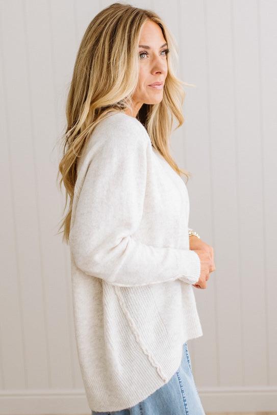 BLONDE WOMAN WEARING A HIGH-LOW HEM, LONG SLEEVE, SUPER SOFT, OVERSIZED CREW NECK SWEATER WITH RIB DETAILS AND STANDING IN A STUDIO WITH LIGHT WOOD FLOOR AND PANELED WALL BEHIND.