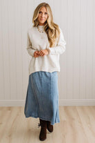 BLONDE WOMAN WEARING A HIGH-LOW HEM, LONG SLEEVE, SUPER SOFT, OVERSIZED CREW NECK SWEATER WITH RIB DETAILS AND STANDING IN A STUDIO WITH LIGHT WOOD FLOOR AND PANELED WALL BEHIND.