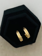 Gold hoop earrings on a black hexagonal stand against a light background