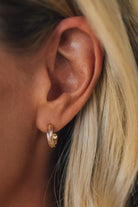 Close-up of an ear wearing a gold hoop earring with blonde hair.