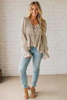 Woman wearing a beige knitted sweater and light blue jeans against a white brick wall.