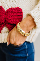 Woman in striped top and light jeans with her hand an a pocket and focused on a large matte gold bangle.