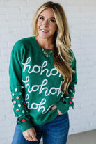 Woman wearing a green sweater with 'ho ho ho' text against a white brick wall.