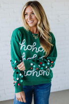 Woman wearing a green sweater with 'ho ho ho' text and colorful polka dots against a white brick wall.