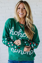 Woman wearing a green sweater with 'ho ho ho' text against a white brick wall.