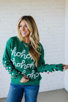 Woman wearing a green sweater with 'ho ho ho' text against a white brick wall.
