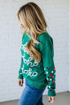 Person wearing a green Christmas sweater with colorful polka dots against a white brick wall.
