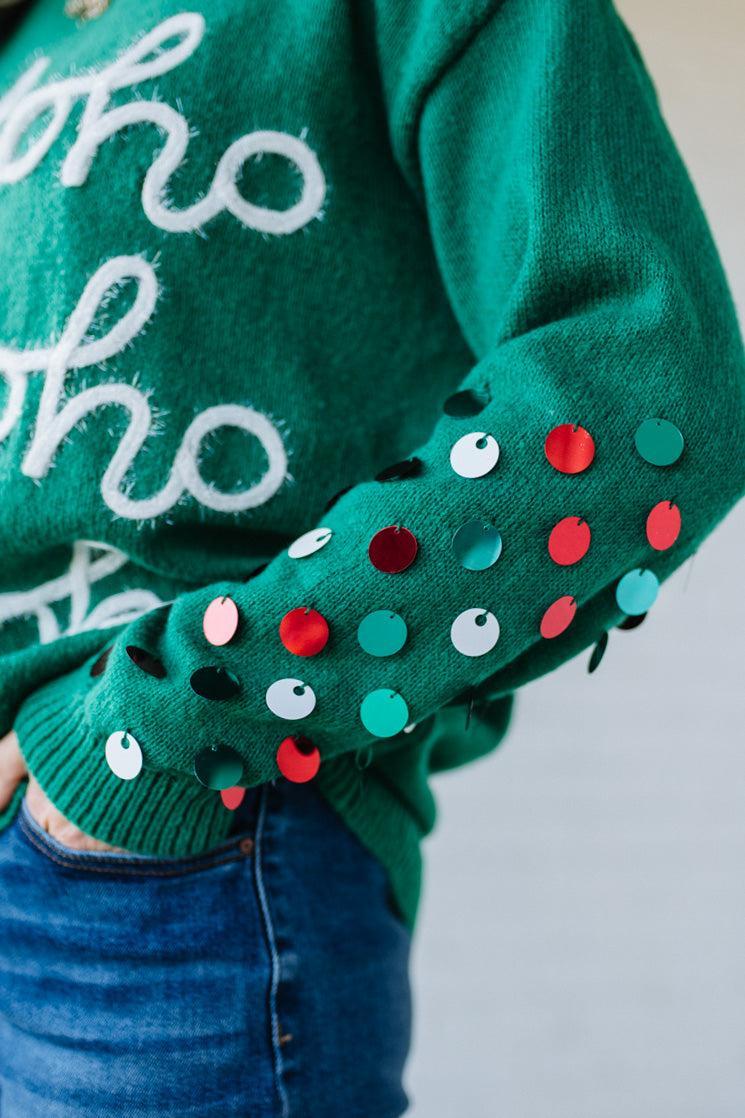 Green sweater with white text and colorful polka dots on sleeves against a neutral background