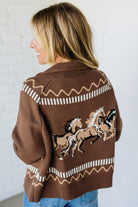 Woman wearing a brown sweater with horse designs against a white background