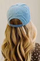 Blonde woman in a brown top showing a denim hat with a brown and white rope across the front, and brown embroidery that says "Not Gonna Hold My Horses"