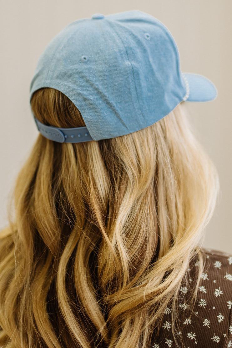 Blonde woman in a brown top showing a denim hat with a brown and white rope across the front, and brown embroidery that says "Not Gonna Hold My Horses"