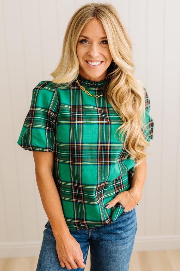 Woman wearing a green plaid top with ruffled sleeves against a neutral background