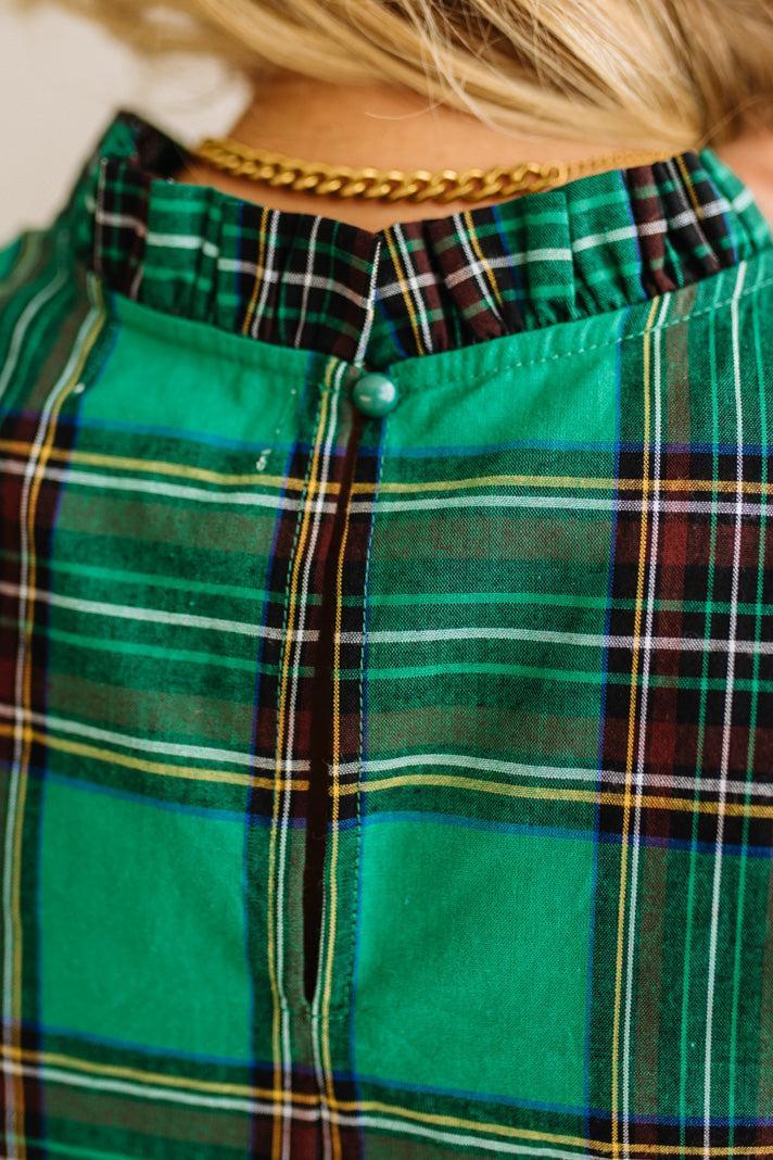 Close-up of a green plaid shirt with a gold necklace.