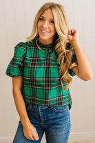 Woman wearing a green plaid top and blue jeans against a neutral background