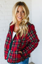 Woman wearing a red plaid jacket against a white brick wall