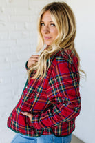 Woman wearing a red plaid jacket against a white brick wall.