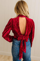 Red velvet top with open back worn by a person against a neutral background