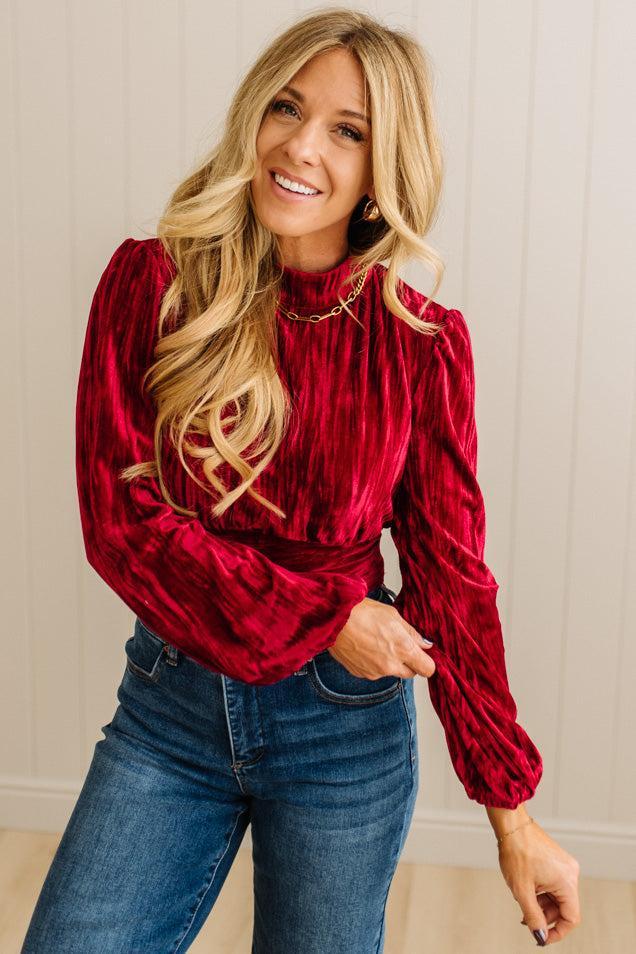 Woman wearing a red velvet top and blue jeans indoors.