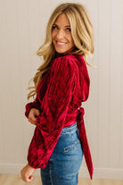 Woman wearing a red velvet top and blue jeans indoors.