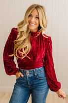 Woman wearing a red velvet top and blue jeans against a neutral background