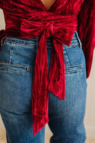 Red velvet top with a tie detail worn over blue jeans on a neutral background