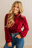 Woman wearing a red velvet top and blue jeans against a neutral background