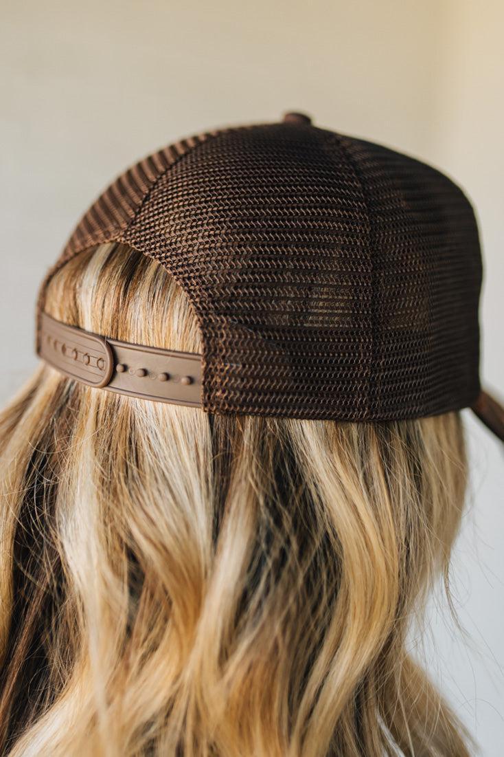 Trucker hat with embroidered design and text held by a person