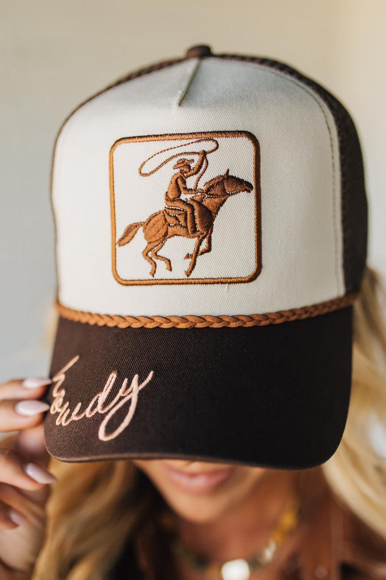Trucker hat with embroidered design and text held by a person