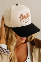 Person wearing a cap with 'Howdy' embroidery on a neutral background