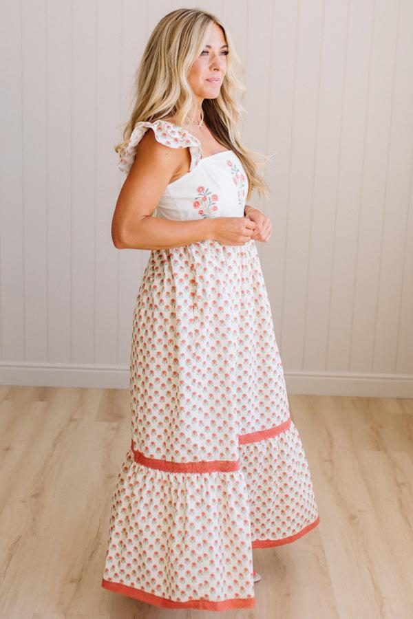 Woman wearing a white dress with red patterns against a light wooden paneled wall.