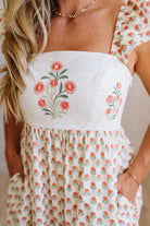 Woman wearing a white dress with floral embroidery and pattern.