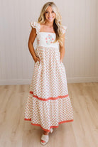 Woman wearing a white dress with floral patterns on a wooden floor.
