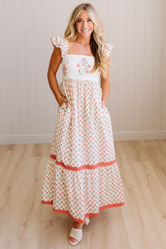 Woman wearing a white dress with floral patterns on a wooden floor.