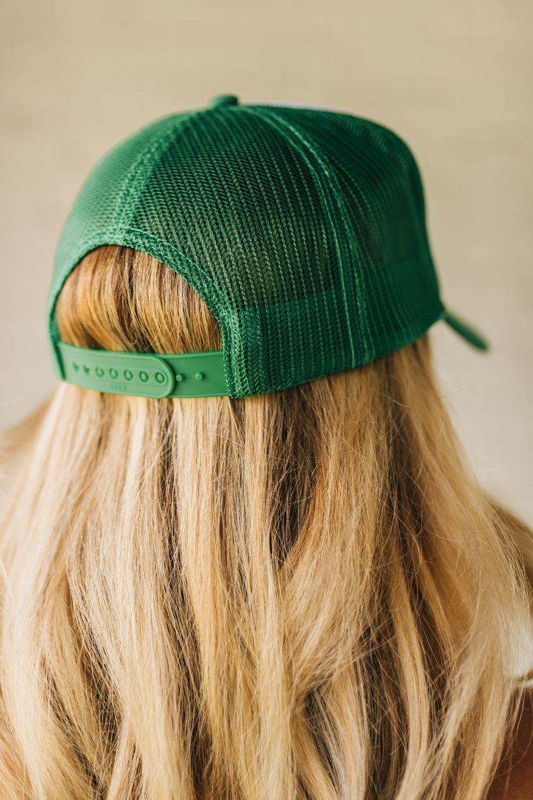 Blonde woman wearing a green mesh back trucker hat with white panel front, and a patch at the center that says "I Will If You Will" with red accent embroidery.