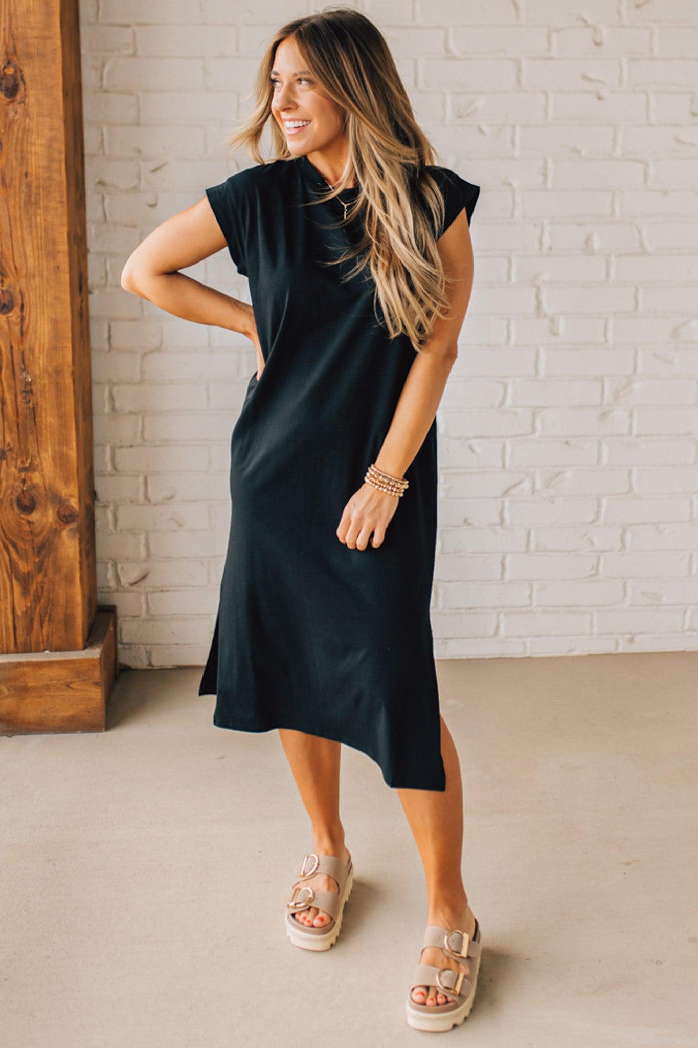 BLONDE WOMAN WEARING A BLACK ROUND NECK SHORT SLEEVE MIDI DRESS WITH SIDE SLIT.