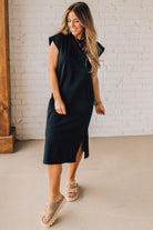 BLONDE WOMAN WEARING A BLACK ROUND NECK SHORT SLEEVE MIDI DRESS WITH SIDE SLIT.