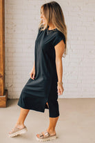 BLONDE WOMAN WEARING A BLACK ROUND NECK SHORT SLEEVE MIDI DRESS WITH SIDE SLIT.