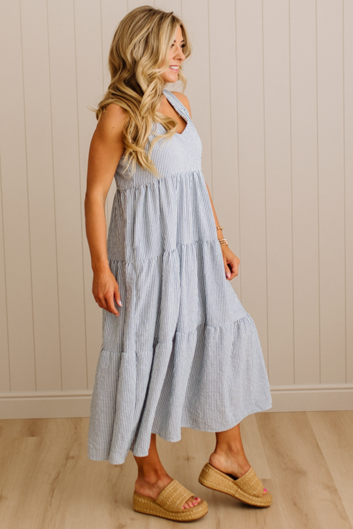 Woman wearing a light gray dress with a white top against a beige wall.