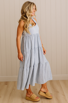Woman wearing a light gray dress with a white top against a beige wall.