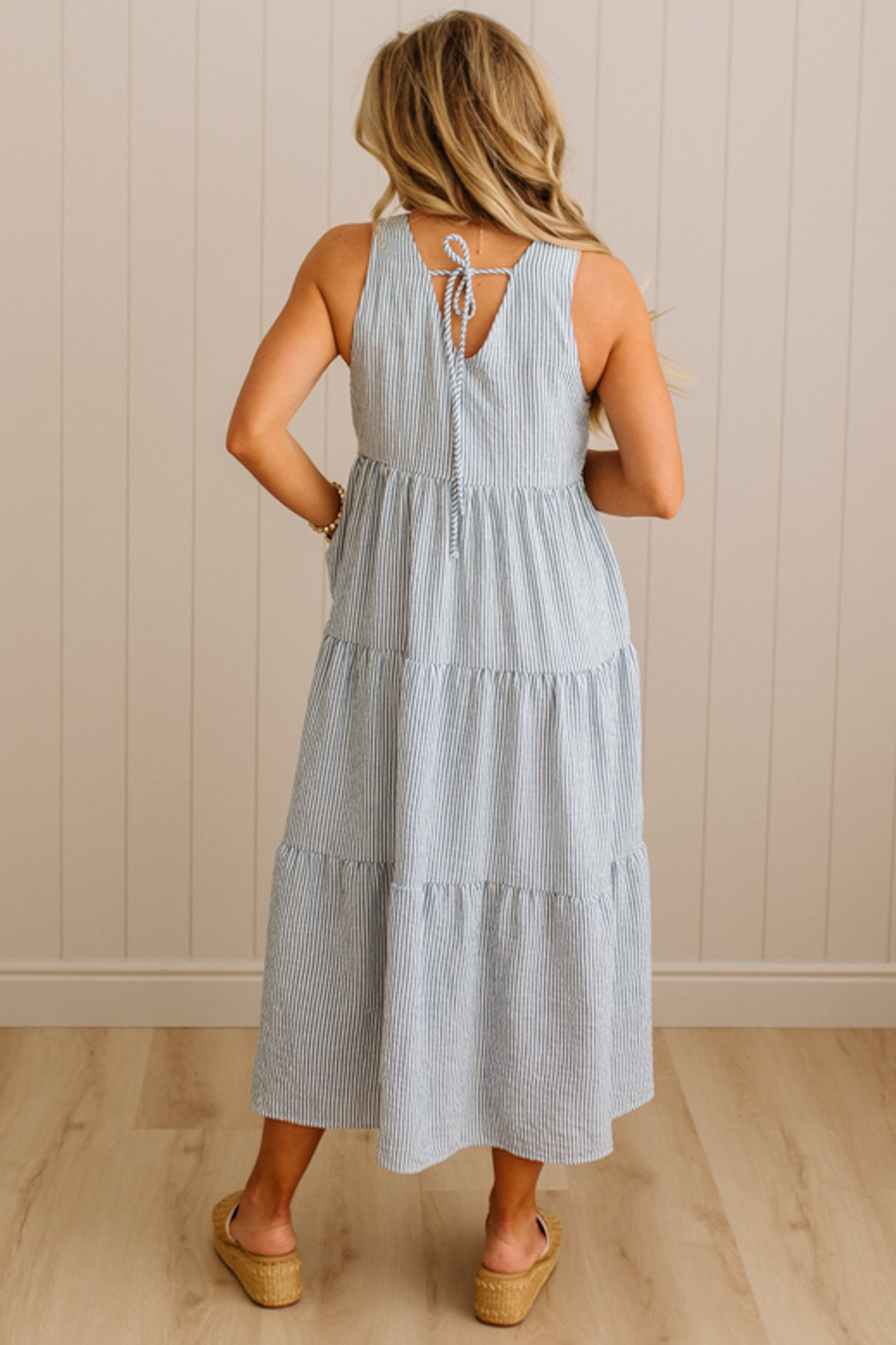 Woman wearing a light blue striped dress with a white wall background