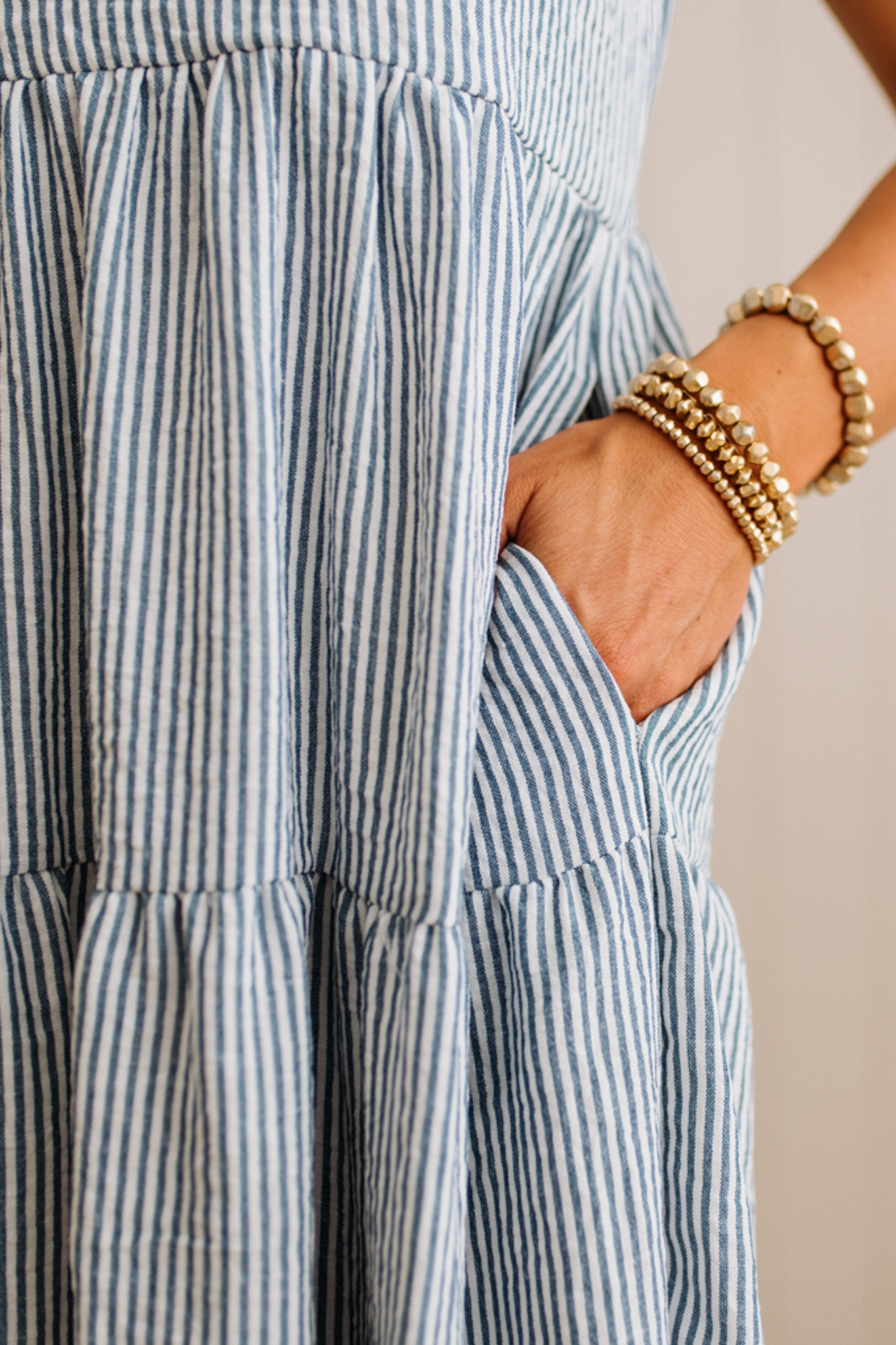 Close-up of a person wearing a blue and white striped dress with hands in pockets, against a neutral background.