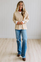 BLONDE WOMAN WEARING A CAMEL AND WHITE STRIPED CREW NECK PULLOVER WITH WHITE AND DARK ORANGE KNIT RIB BAND TRIMMED, IT IS LONG SLEEVED WITH A RELAXED FIT. SHE IS STANDING ON A LIGHT WOOD FLOOR WITH LIGHT BACKGROUND.

