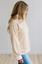 BLONDE WOMAN WEARING A CAMEL AND WHITE STRIPED CREW NECK PULLOVER WITH WHITE AND DARK ORANGE KNIT RIB BAND TRIMMED, IT IS LONG SLEEVED WITH A RELAXED FIT. SHE IS STANDING ON A LIGHT WOOD FLOOR WITH LIGHT BACKGROUND.
