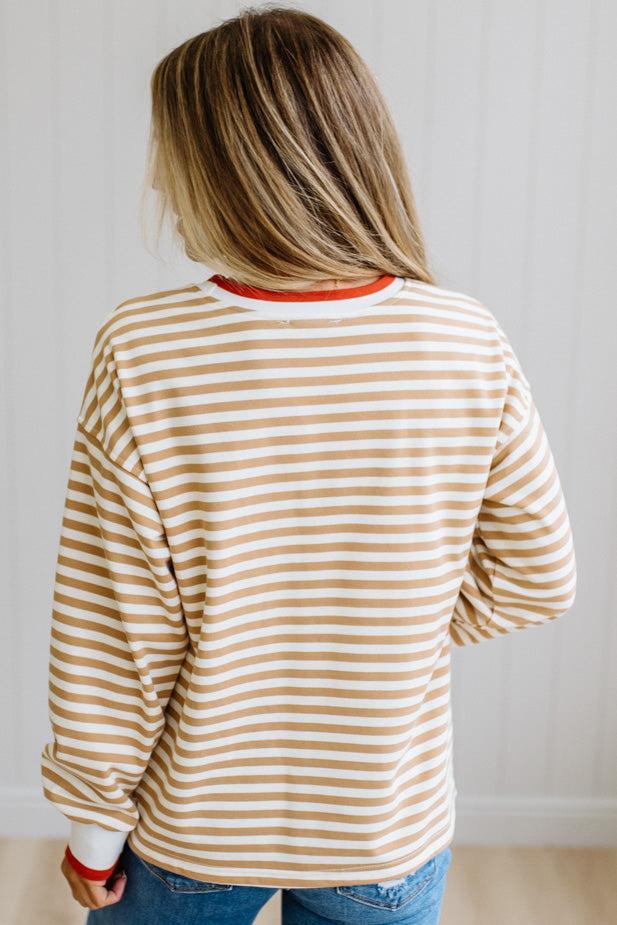 BLONDE WOMAN WEARING A CAMEL AND WHITE STRIPED CREW NECK PULLOVER WITH WHITE AND DARK ORANGE KNIT RIB BAND TRIMMED, IT IS LONG SLEEVED WITH A RELAXED FIT. SHE IS STANDING ON A LIGHT WOOD FLOOR WITH LIGHT BACKGROUND.
