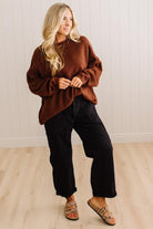 A woman modeling a brown fuzzy knit sweater, black wide-leg pants, and leopard-print flat shoes in a bright room with light wood floors and white paneled walls.