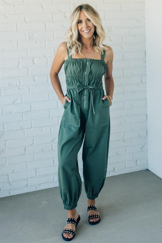 Women wearing olive green jumpsuit with elastic waist and front zipper.