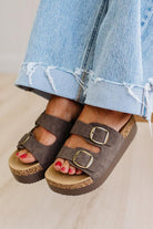 Brown sandals with buckles worn with light blue jeans on a neutral background